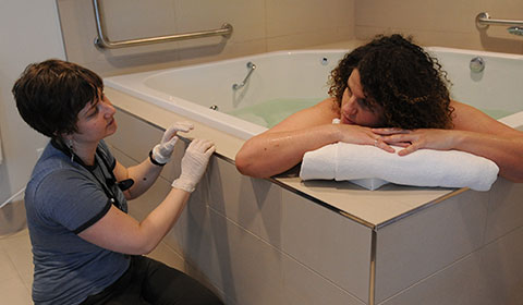 Photo of a labouring person in birth pool chatting with their midwife at a birth centre.