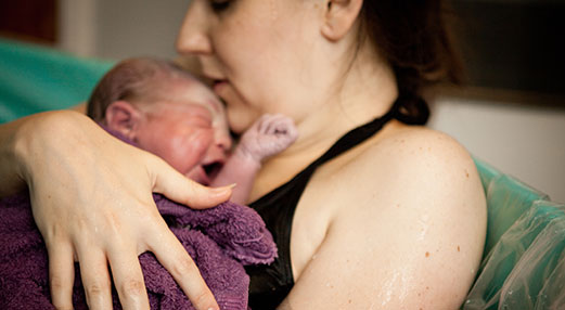 Picture of a woman in birth pool holding newborn.