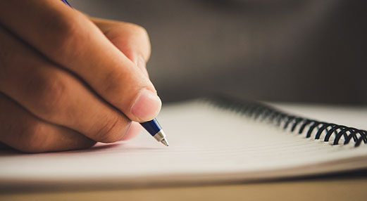 Photo of a hand writing in a notebook.