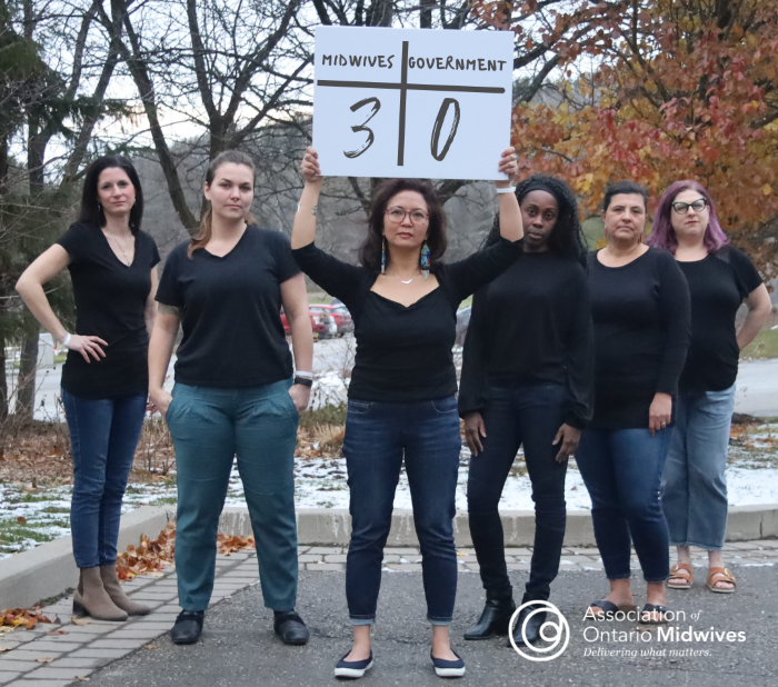 Members of the A-O-M board hold up a scorecard that reads "Midwives: 3, government: 0"