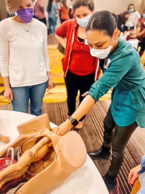 Three individuals practice emergency childbirth skills with model torso and infant doll.