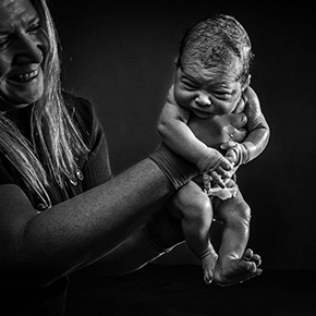 Midwife smiling, holding up newborn